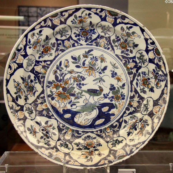 Ceramic shallow bowl (c1730) with center decoration of Chinese style bird on a rock & on-rim medallions of Christian symbol of three entwined fish, likely made in Bristol, at Bristol Museum & Art Gallery. Bristol, England.