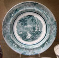 Underglaze-printed plate green with exotic hunting scene & Celtic interlace border made by Bristol Pottery at Bristol Museum & Art Gallery. Bristol, England.